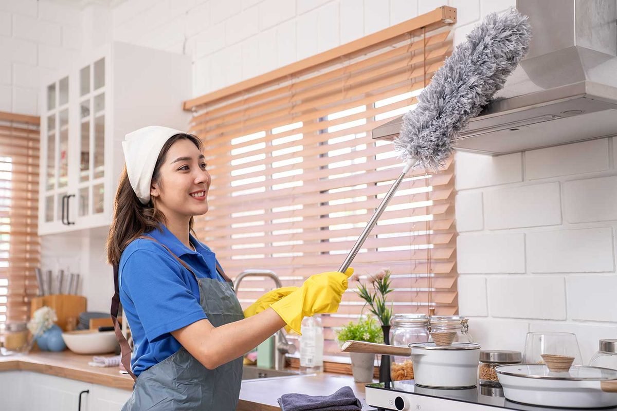 Cleaner dusting a kitchen range hood and window blinds